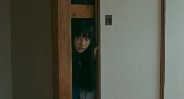 暗い部屋で身をすくめ、怯える表情を見せる章子(山﨑七海)