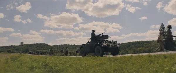 一本道を歩く少年たちの背後から軍用車両が監視する映画『ロングウォーク』のワンシーン