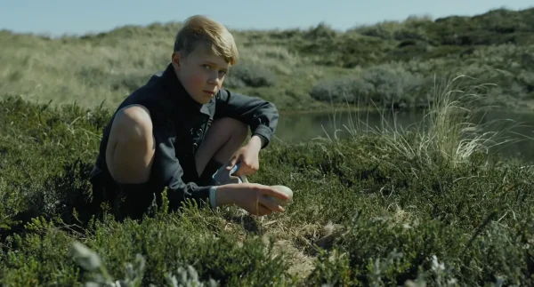 厳格なナチズム思想を持つ母親の重圧を受けながら、不安と強い意志を宿した青い瞳で正面を見つめるナニングの表情のクローズアップ